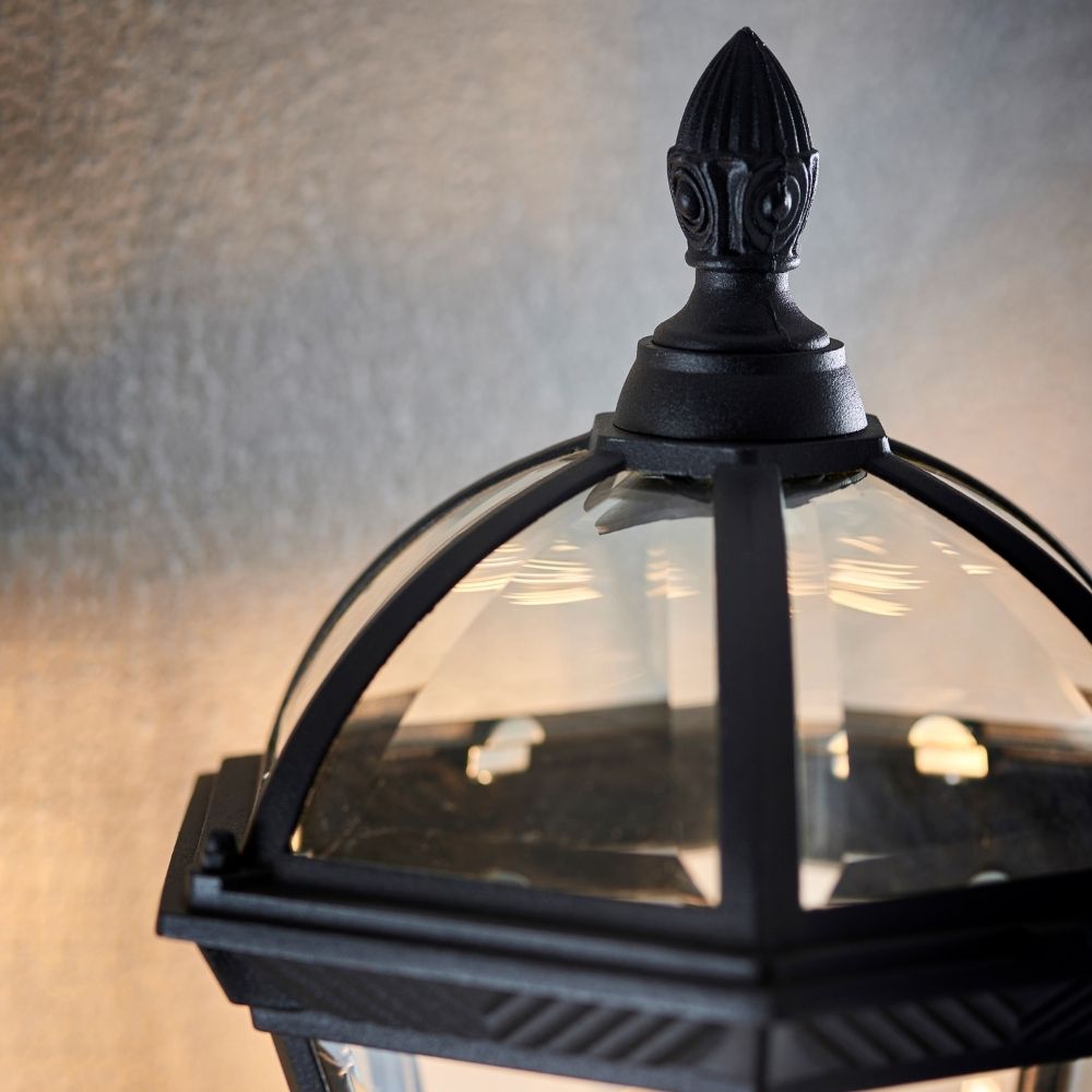 Close up of black wall lantern showing decorative finial and curved glass dome detail.