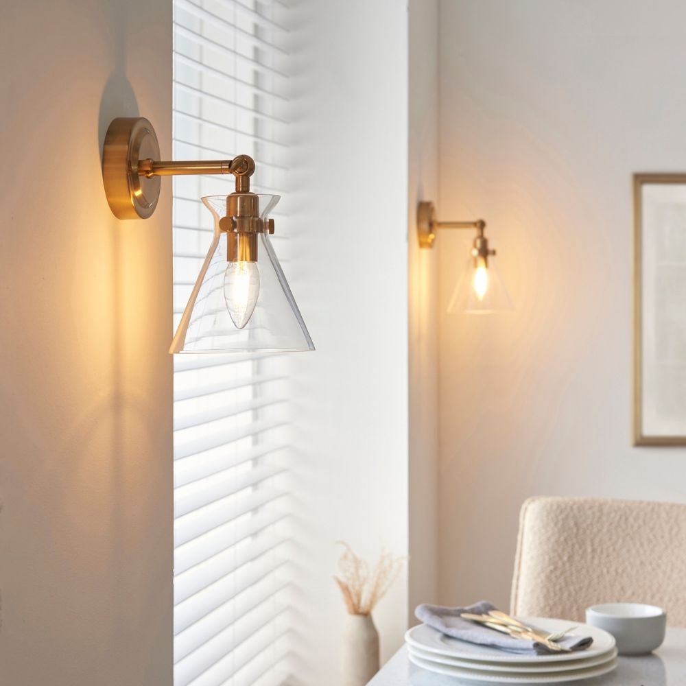 Pair of adjustable brass wall lights with clear glass shades illuminating a contemporary dining or living space.
