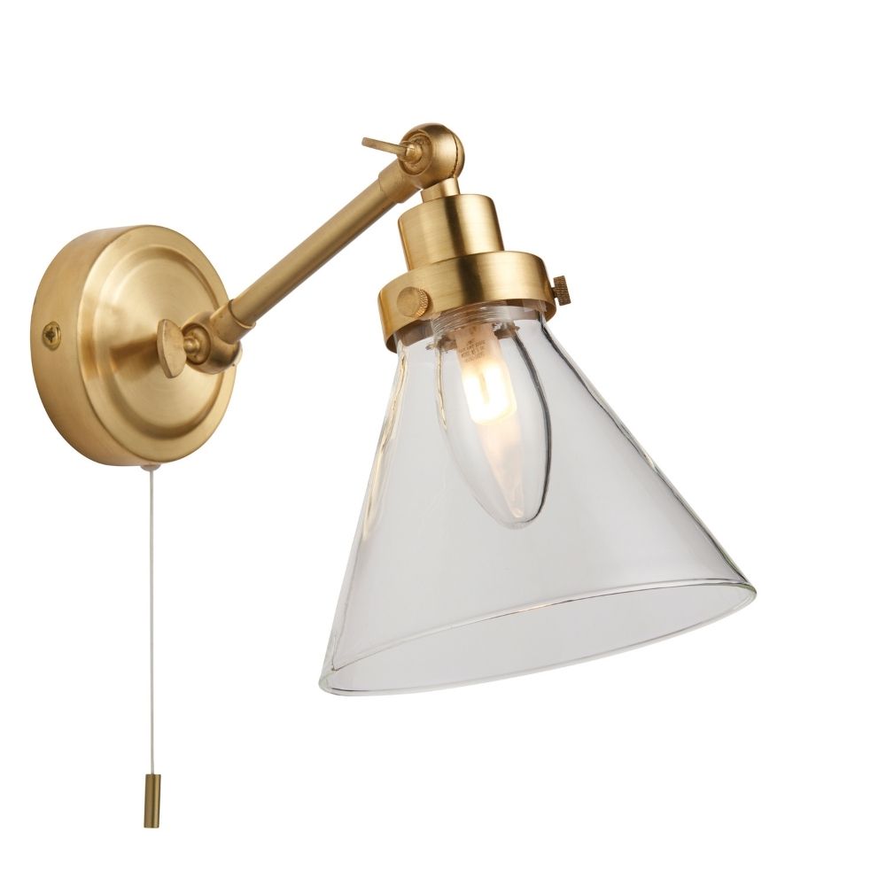 Aged brass wall light featuring a clear cone-shaped glass shade and exposed bulb on a neutral background.