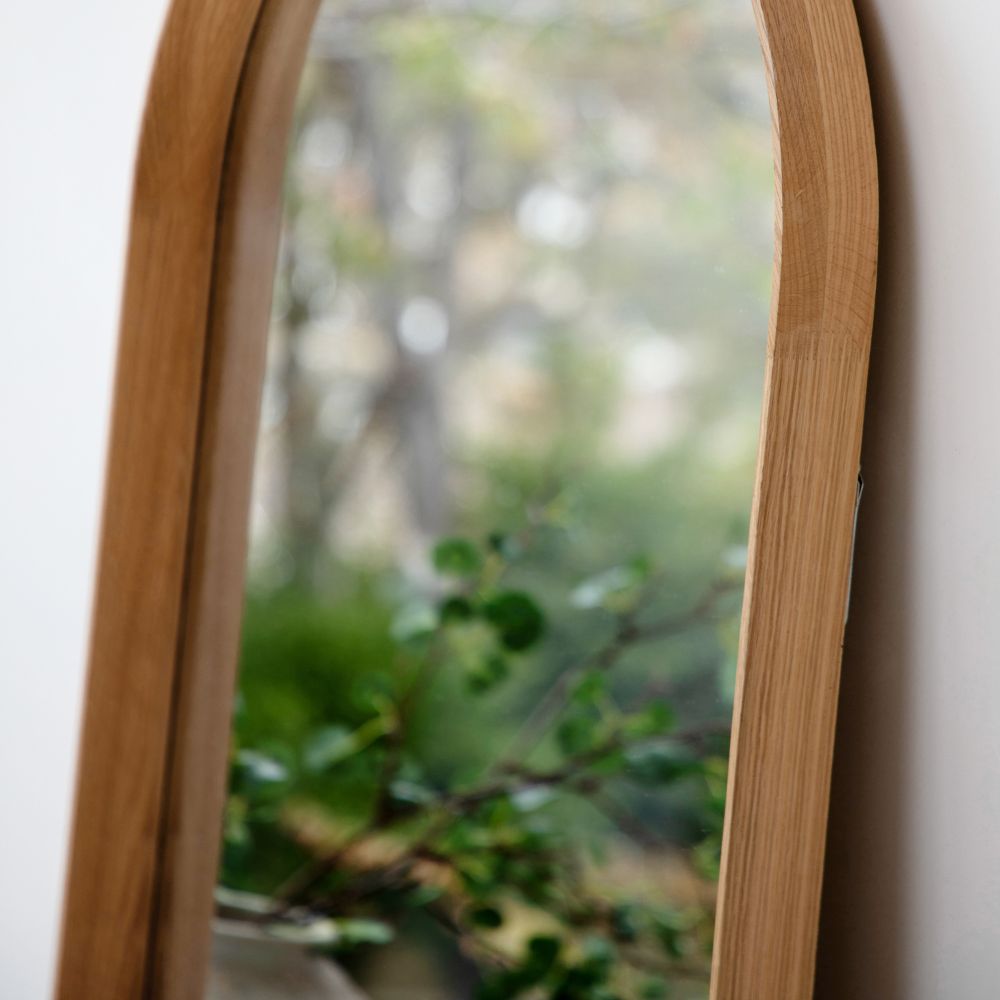 Angled close-up of a slim natural oak frame on an arched full length mirror with smooth handcrafted detailing.
