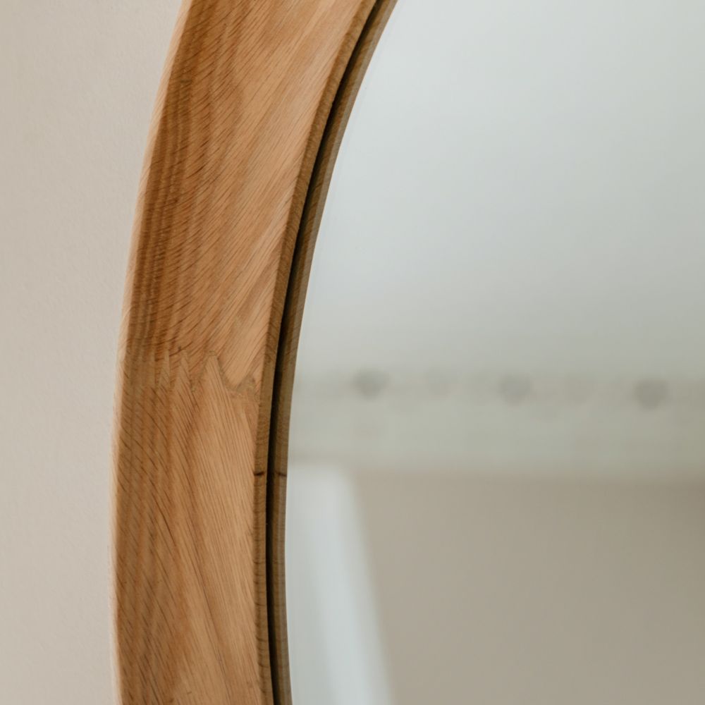 Angled close-up of a handcrafted oak wall mirror frame showing natural wood texture and curved organic shaping.