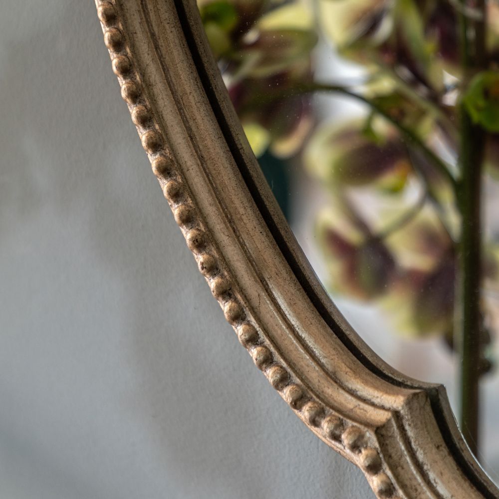 Close-up detail of a scalloped antique gold mirror frame featuring ornate beaded trim and an aged metallic finish.
