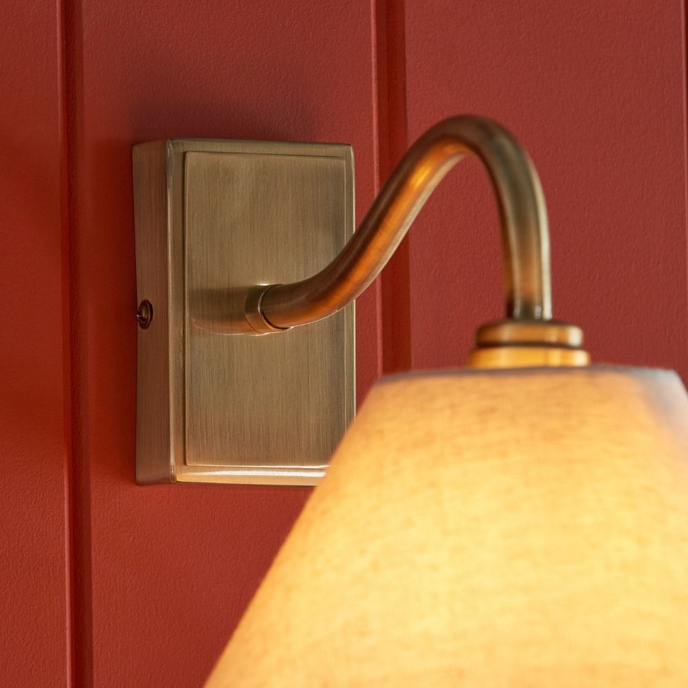 Close up of antique brass wall light backplate and curved arm showing brushed finish and mounting detail.