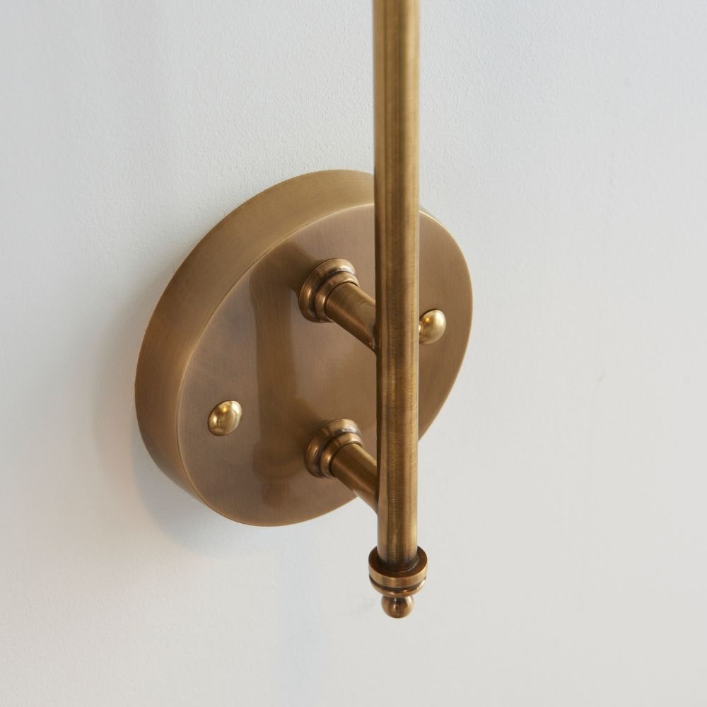 Close up of antique brass wall light showing circular backplate, mounting arms, and brushed metal finish detail.