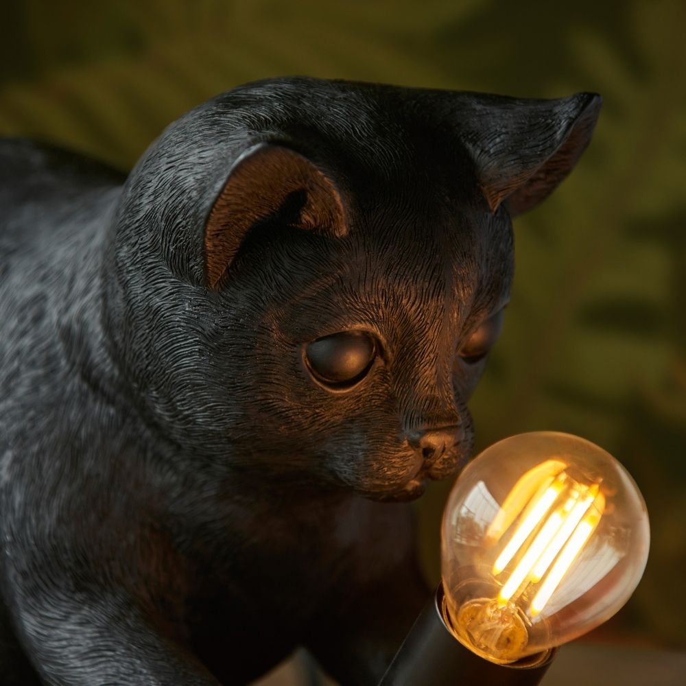 Close-up of black cat resin lamp highlighting detailed fur texture and glowing filament bulb, emphasising craftsmanship and warm lighting effect.