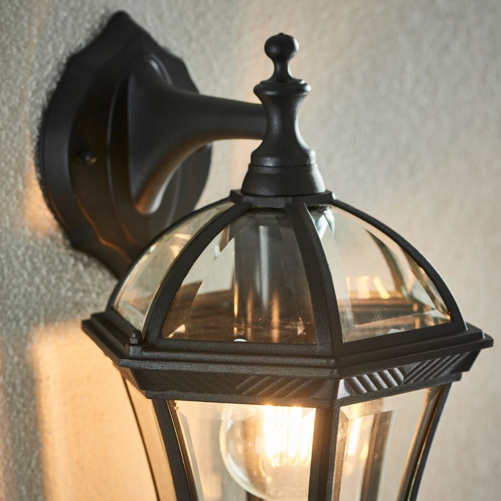 Close up of black outdoor wall lantern showing glass dome, metal frame, and decorative finial detail.