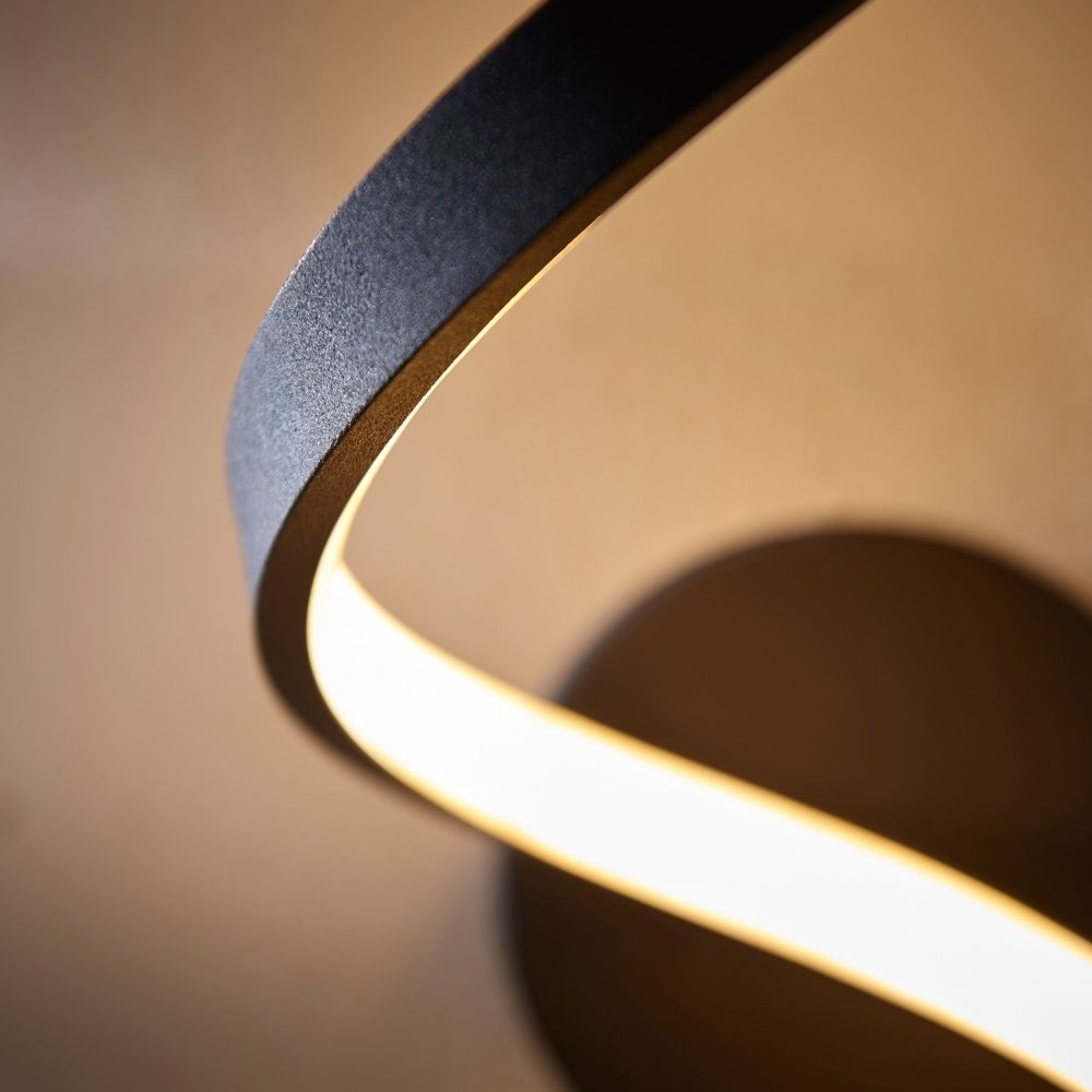 Close up of black twisted LED wall light showing curved aluminium structure and glowing light strip.