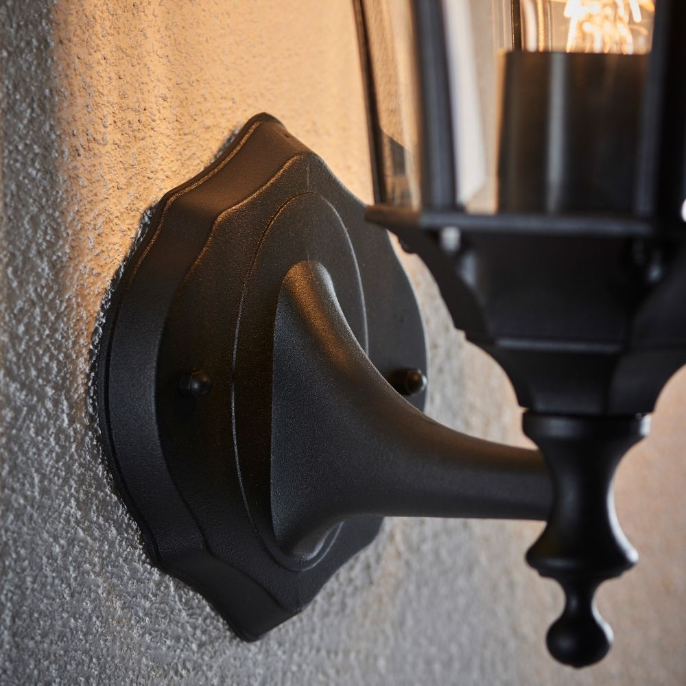 Close up of black outdoor wall lantern mounting bracket and arm attached to textured exterior wall.