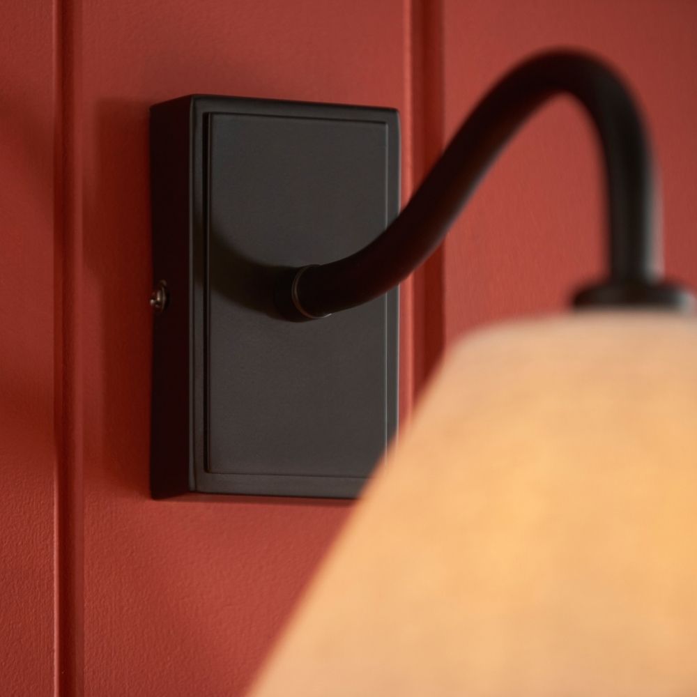 Close up of black wall light backplate and curved arm showing smooth matte finish and mounting detail.