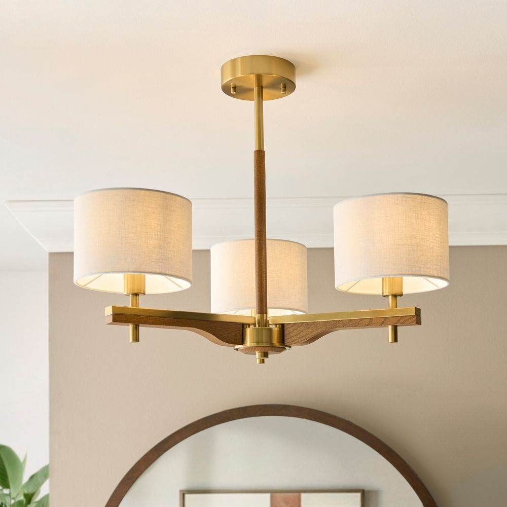 Brass and ash wood semi flush ceiling light with three linen fabric shades in a modern interior setting.