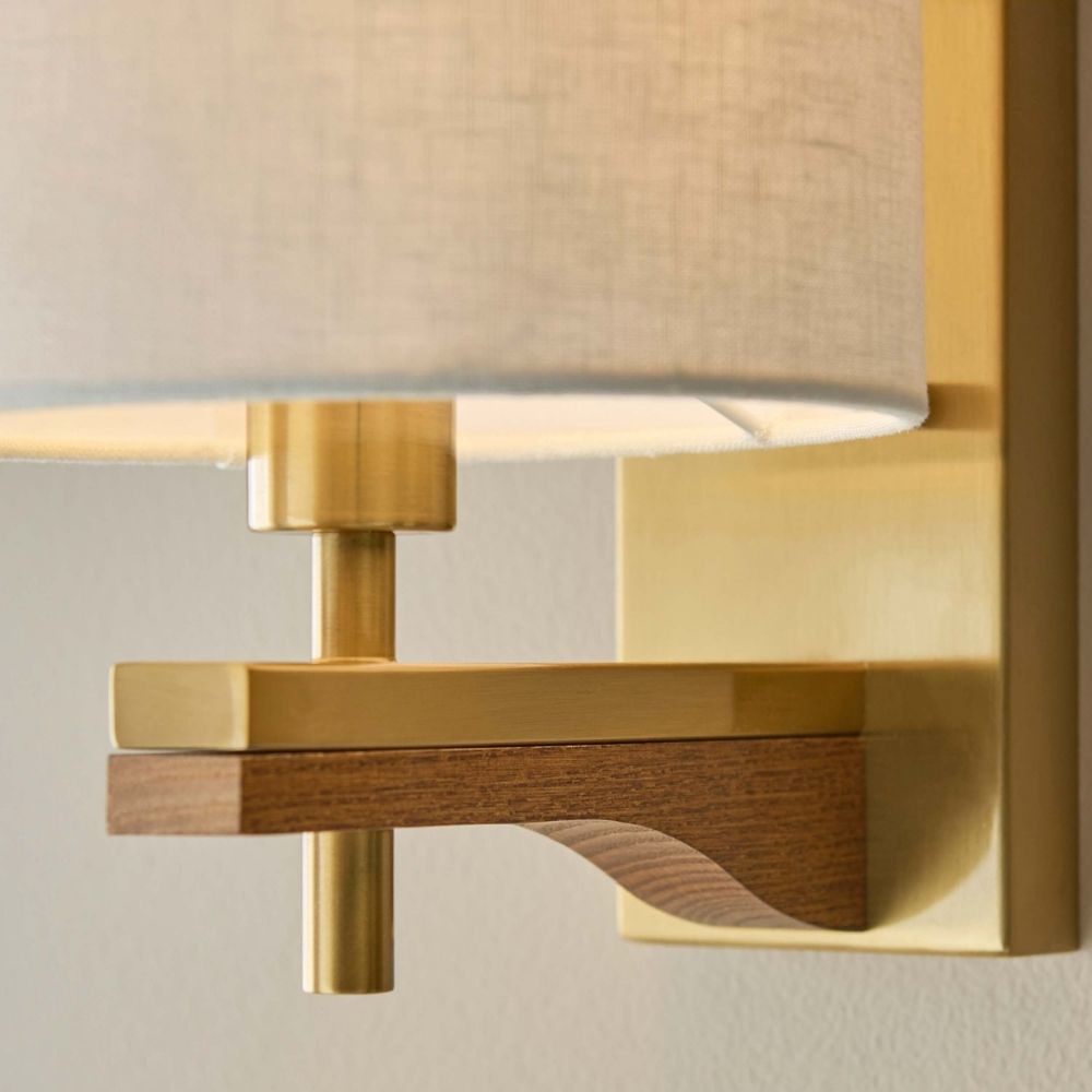 Close-up of brass wall light showing ash wood detail, metal fittings and linen shade texture.