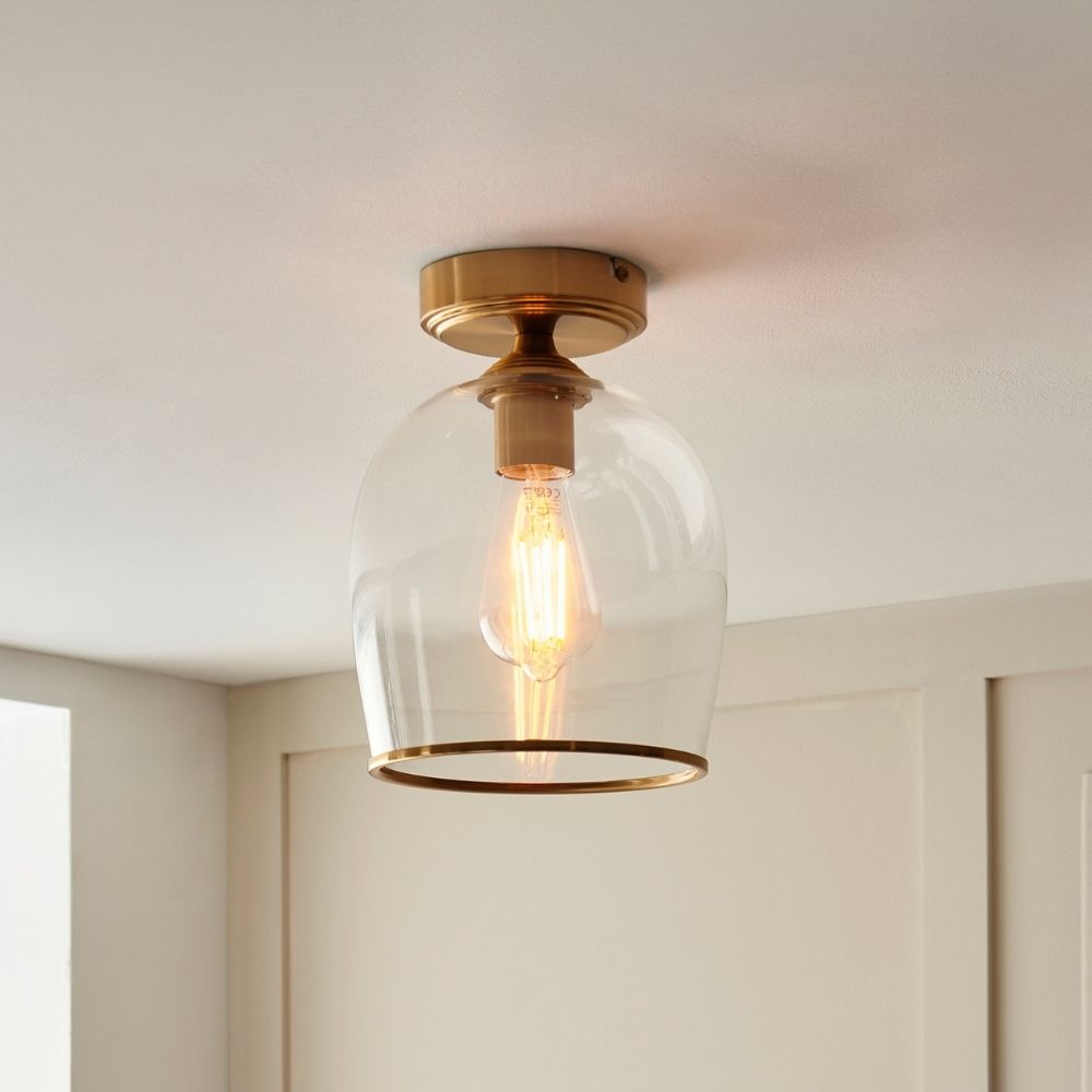 Modern ceiling light with a brass fitting and clear glass dome shade featuring an exposed filament bulb.