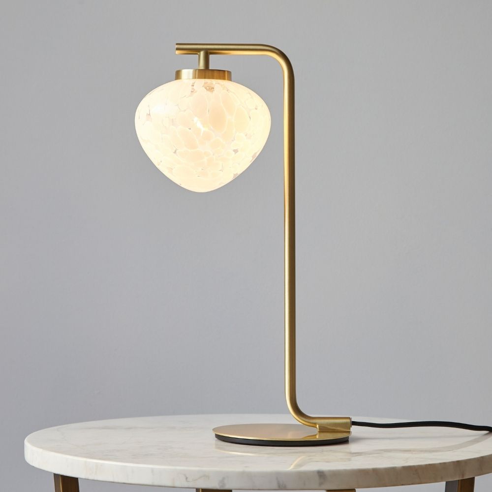 Modern brass and glass decorative table lamp with curved stem and textured glass shade, styled on a marble side table for contemporary interior lighting.