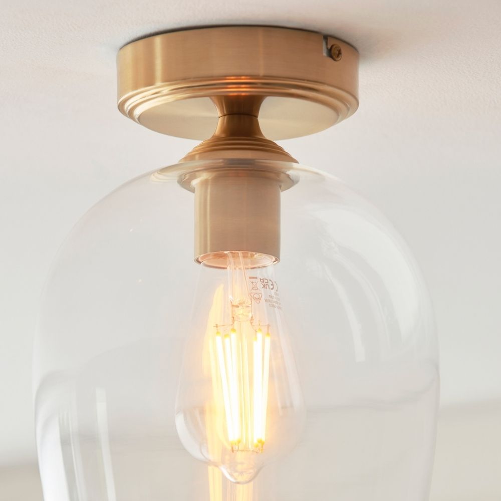 Close-up of brass ceiling light fitting and clear glass shade showing warm glowing filament bulb.