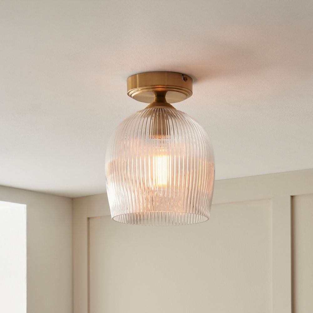Brass flush ceiling light with ribbed glass shade and warm ambient glow in a modern interior setting.