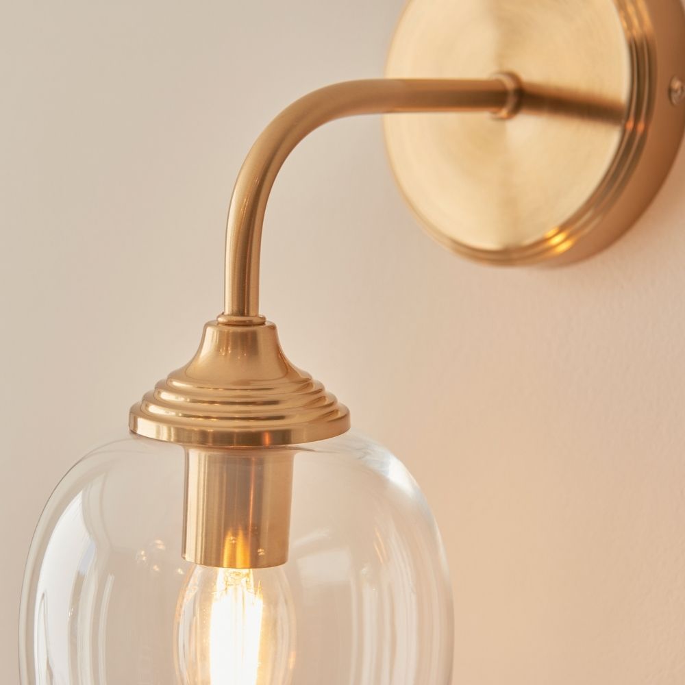 Close-up of aged brass wall light arm and circular backplate, showcasing smooth curved design and brushed metallic finish.