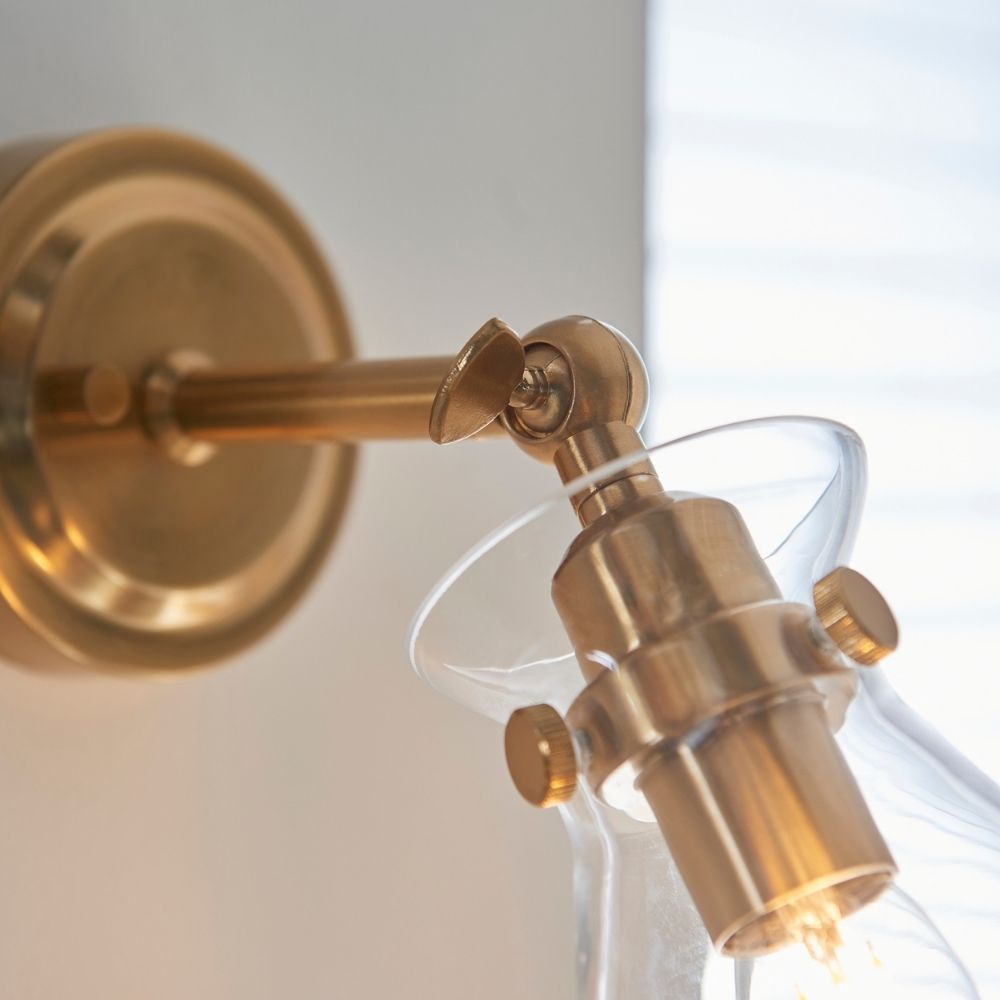Close-up of brass adjustable wall light showing pivot joint, fittings and clear glass shade detail.