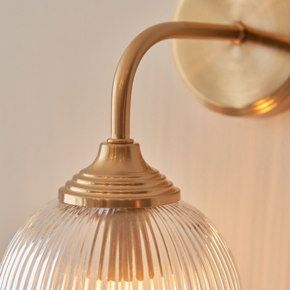 Detailed view of aged brass wall light arm and mounting plate, showcasing curved design and metallic finish.