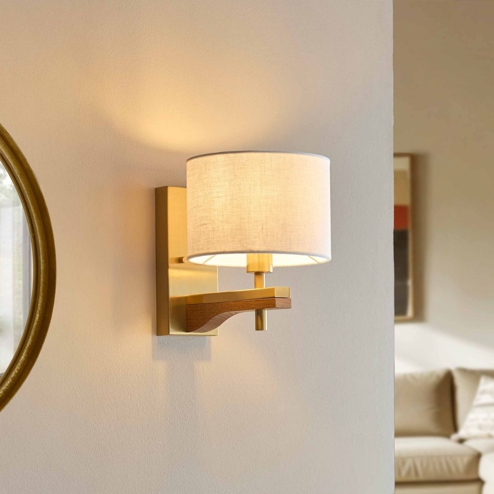 Brass wall light with linen shade and ash wood detail mounted on a neutral wall in a warm contemporary interior setting.