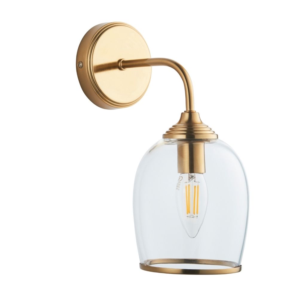 Wall-mounted brass sconce featuring a curved arm and clear domed glass shade with visible filament bulb, isolated on white background.