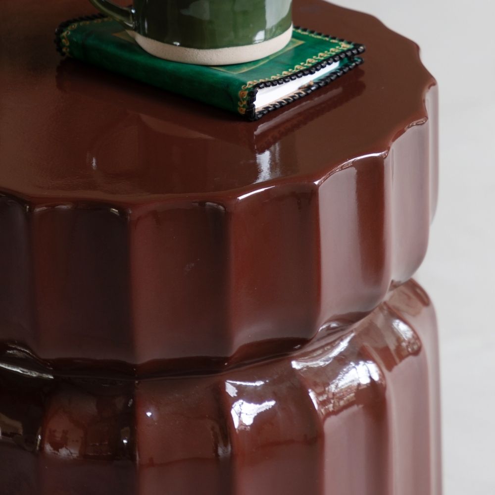 Close up of brown ridged side table showing glossy finish and textured fluted edges with styled accessories on top.