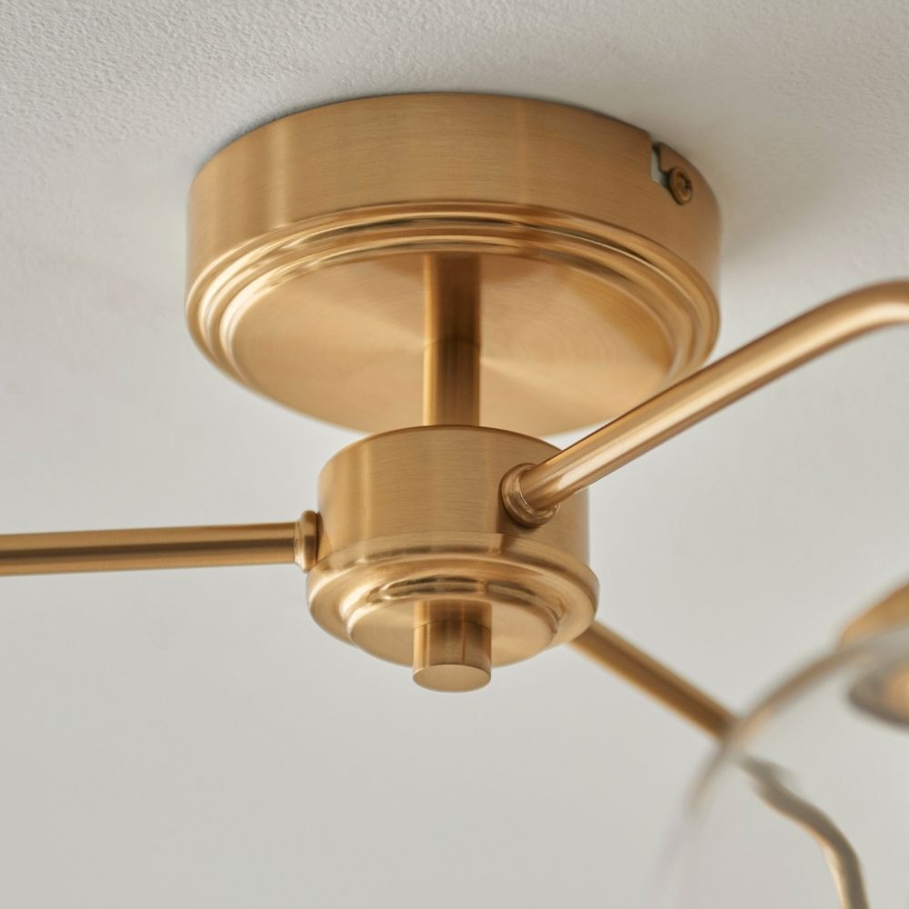 Detailed view of the brushed brass ceiling mount and connecting arms of a three light ceiling fixture.