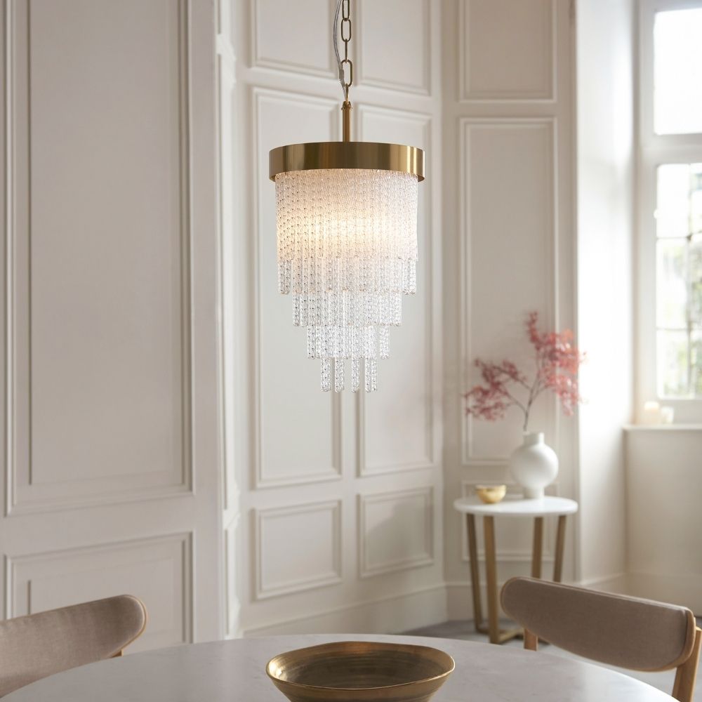 Brushed brass pendant ceiling light with cascading tiered glass drops creating a soft warm glow in a dining room setting.
