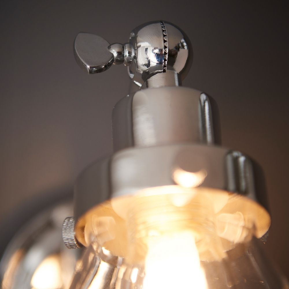 Close-up of chrome wall light showing adjustable joint and fittings above the clear glass shade and illuminated bulb.