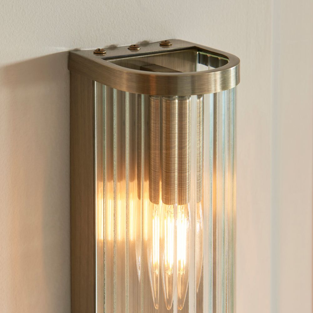 Close-up detail of an antique brass wall sconce with ribbed glass casing and illuminated filament bulb for decorative lighting.