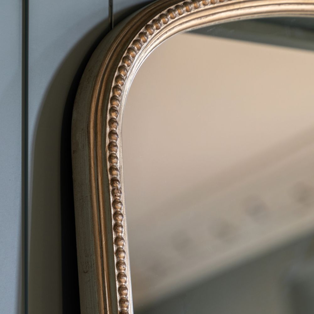 Close-up detail of an arched antique gold mirror frame featuring decorative beaded trim and a vintage metallic finish.