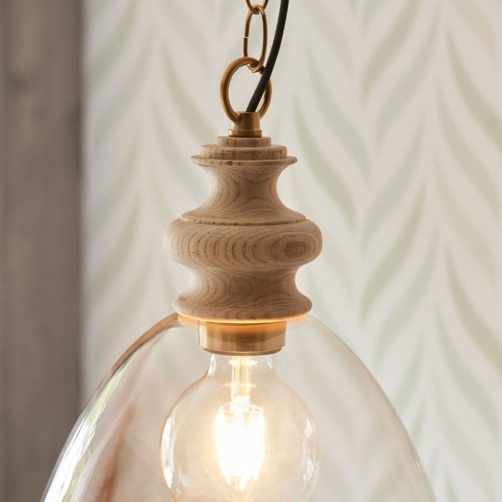 Close up of ash wood pendant light fitting with visible grain detail, brass accents and illuminated exposed bulb.