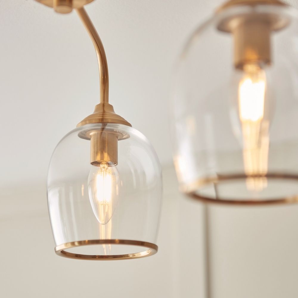 Close up of brass ceiling light arm and clear glass shade highlighting the warm glowing filament bulb.