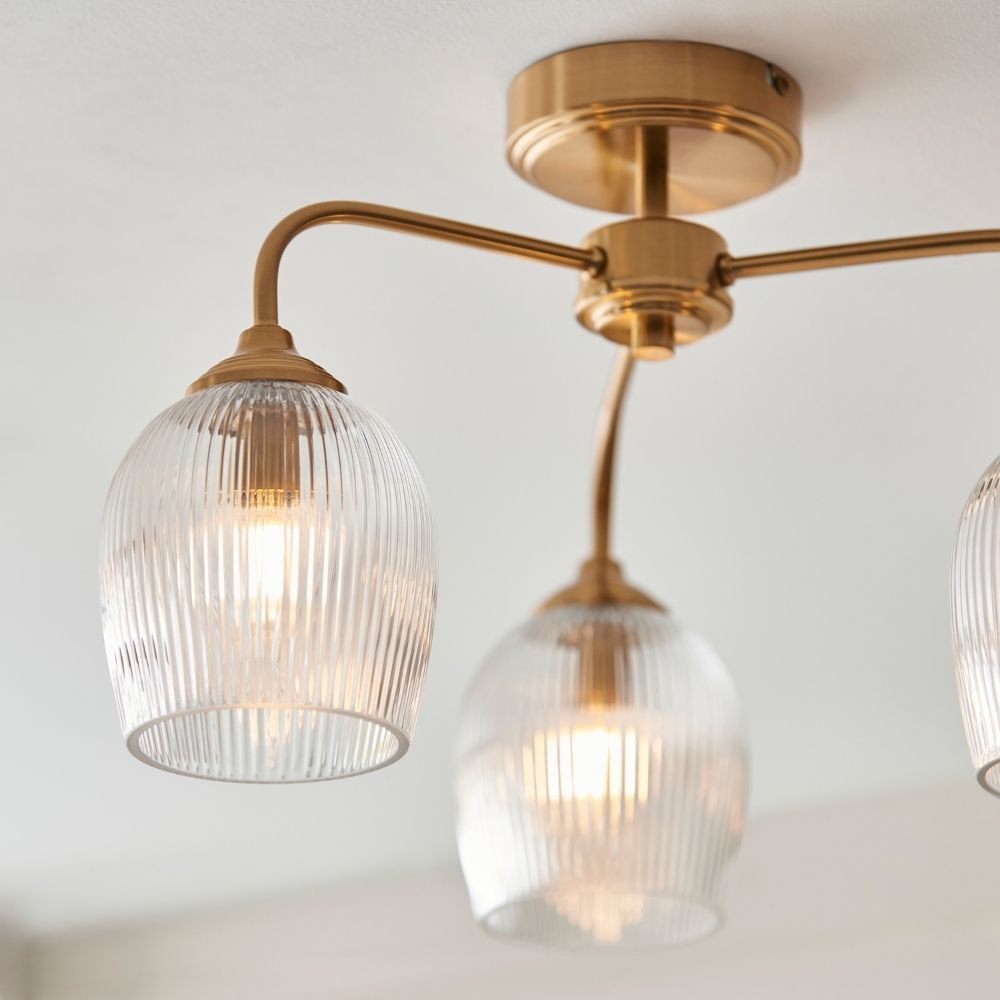 Close up of brass ceiling light arm and ribbed glass shade with softly glowing filament bulb.