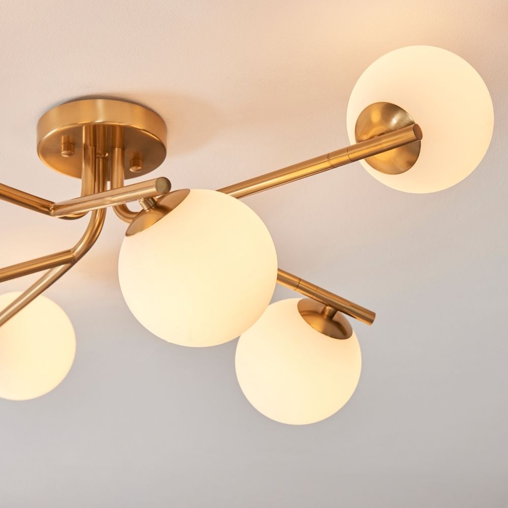 Close up of brass ceiling light showing frosted glass globe shades and sleek mid century metal arm design.