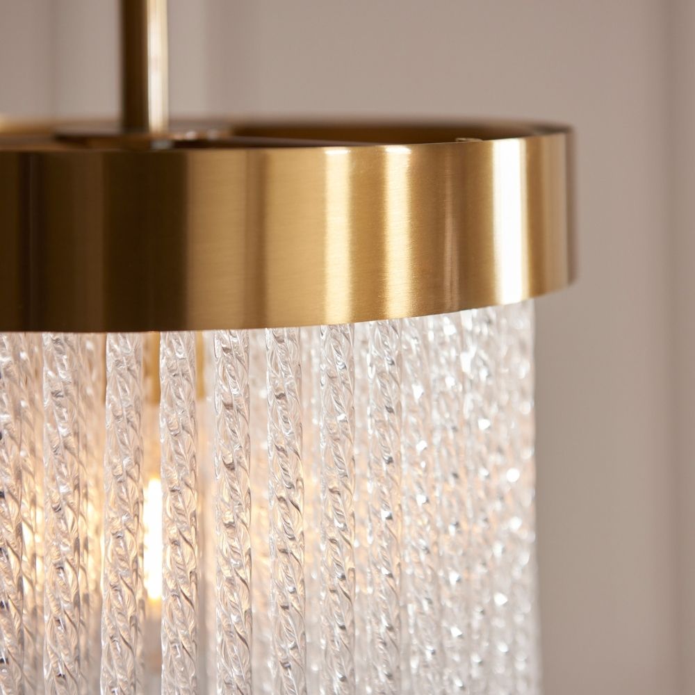Close up of brushed brass ceiling light rim with textured glass drop elements reflecting warm light.