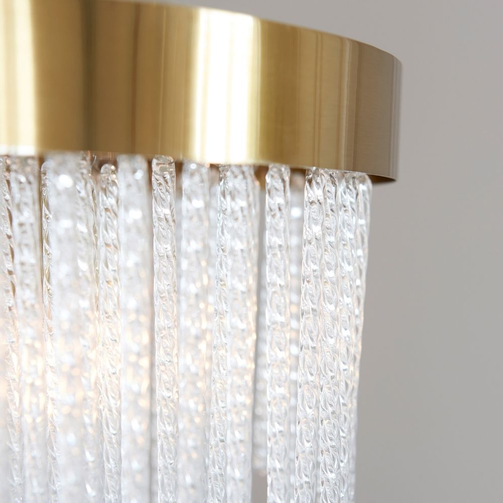 Detailed close up of brushed brass light fitting with vertically hanging textured glass rods reflecting warm illumination.