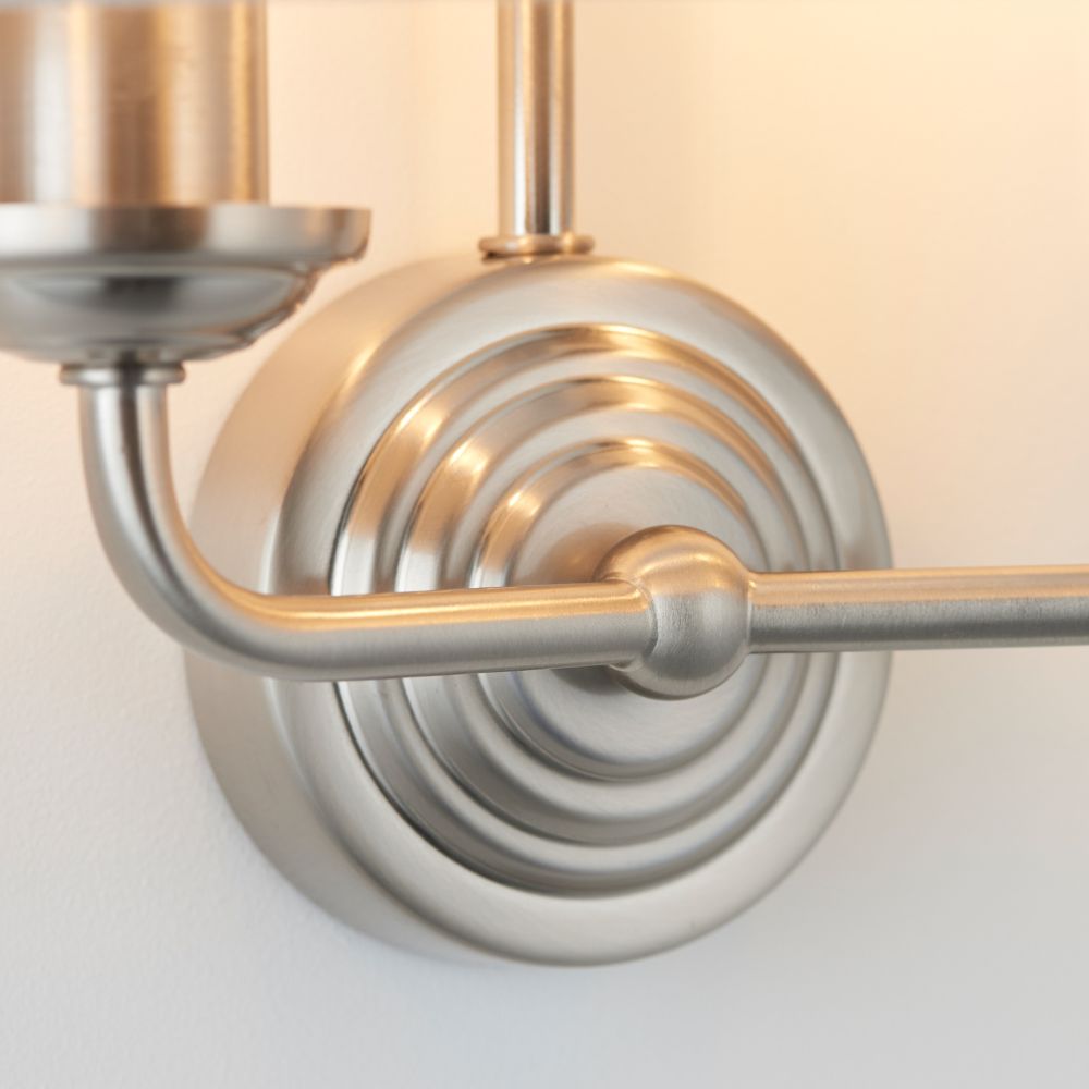Close-up detail of a brushed steel wall light fitting with curved arm design and polished circular backplate.