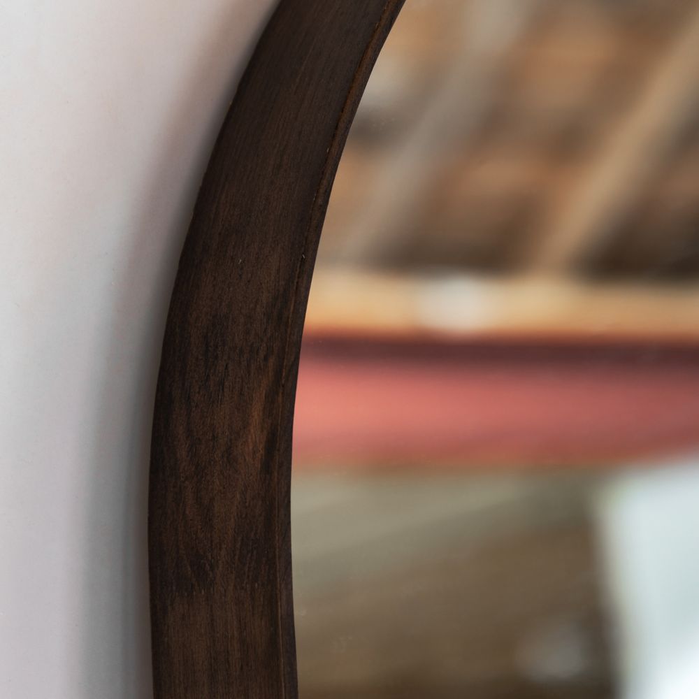 Close-up detail of a dark stained wooden frame on an arched full length mirror showing natural grain and curved edges.