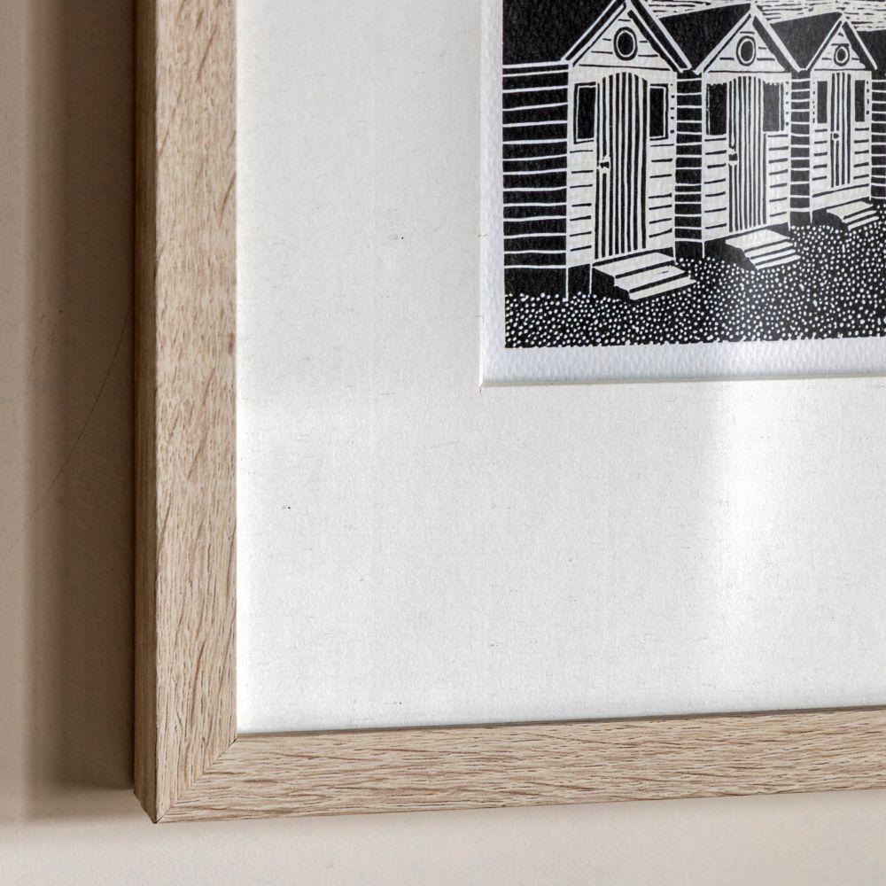 Close-up detail of a natural wood-effect picture frame with textured mount surrounding a monochrome coastal artwork.