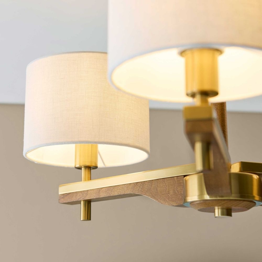Close up of linen lampshade and brushed brass arm on a wooden semi flush ceiling light fitting.
