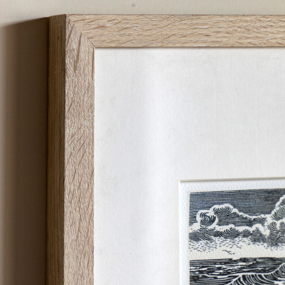 Detailed close-up of framed beach hut linocut print with natural oak-effect frame and neutral textured mount.
