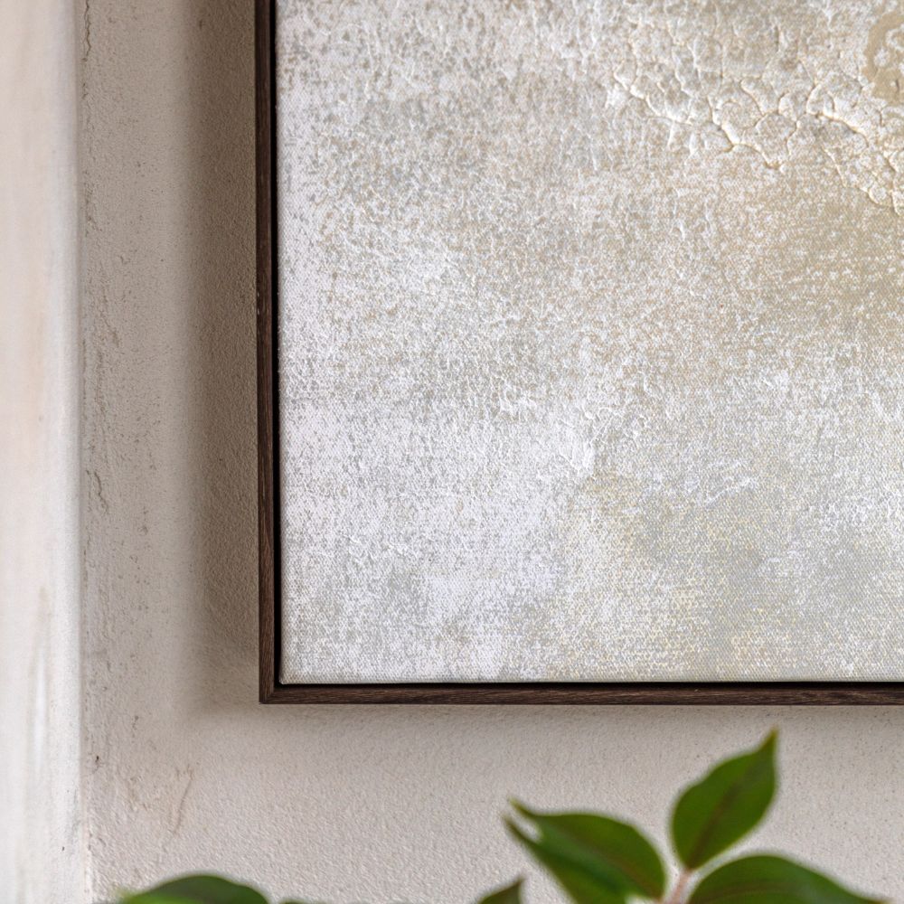 Close-up detail of neutral abstract canvas artwork showing textured paint surface and slim dark wood frame.