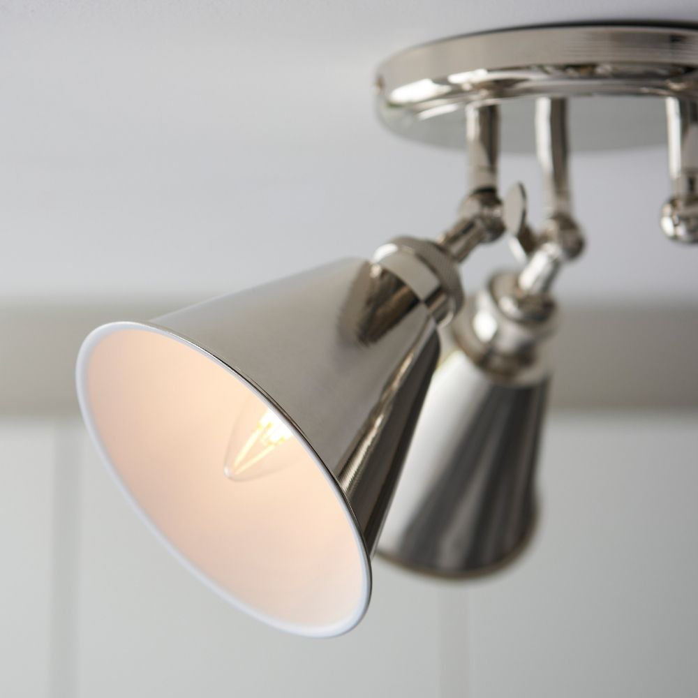 Close up detail of polished nickel adjustable spotlight head with warm glowing bulb and reflective finish.