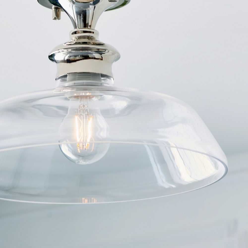 Close up of polished nickel ceiling light with transparent glass dome highlighting exposed filament bulb detail.