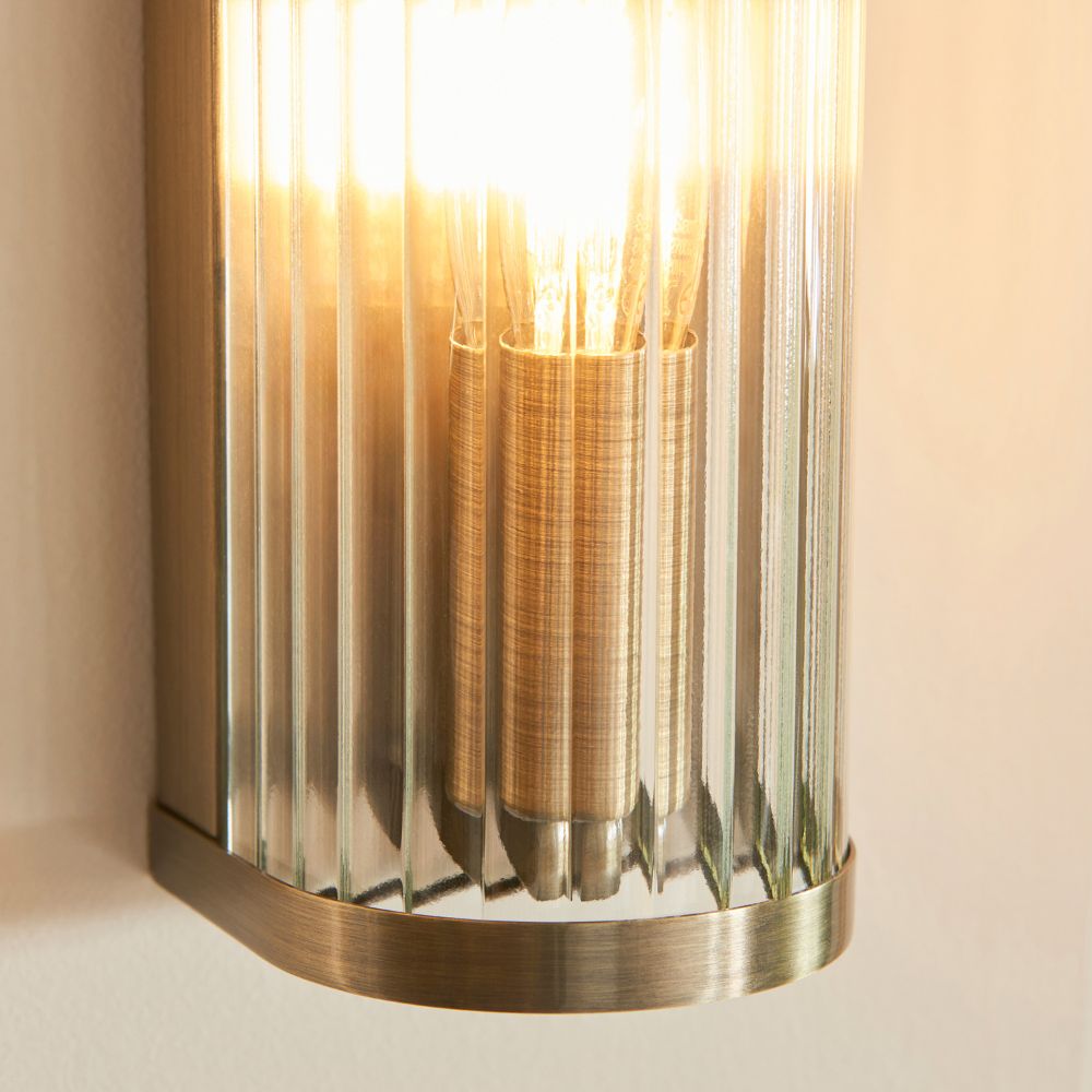 Close-up detail of a brass wall light with ribbed glass surround and illuminated filament bulb creating a warm glow.