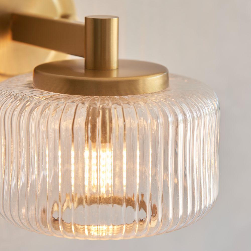 Close-up of a ribbed glass wall light with brushed brass detailing and warm glowing bulb inside.