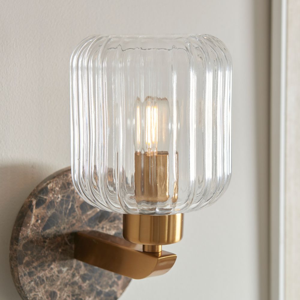 Close-up of a ribbed glass wall light with brushed brass detailing and softly illuminated bulb for modern interiors.