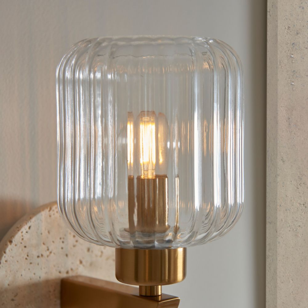 Close-up of a ribbed glass wall light with warm brass detailing and softly illuminated bulb for modern interiors.
