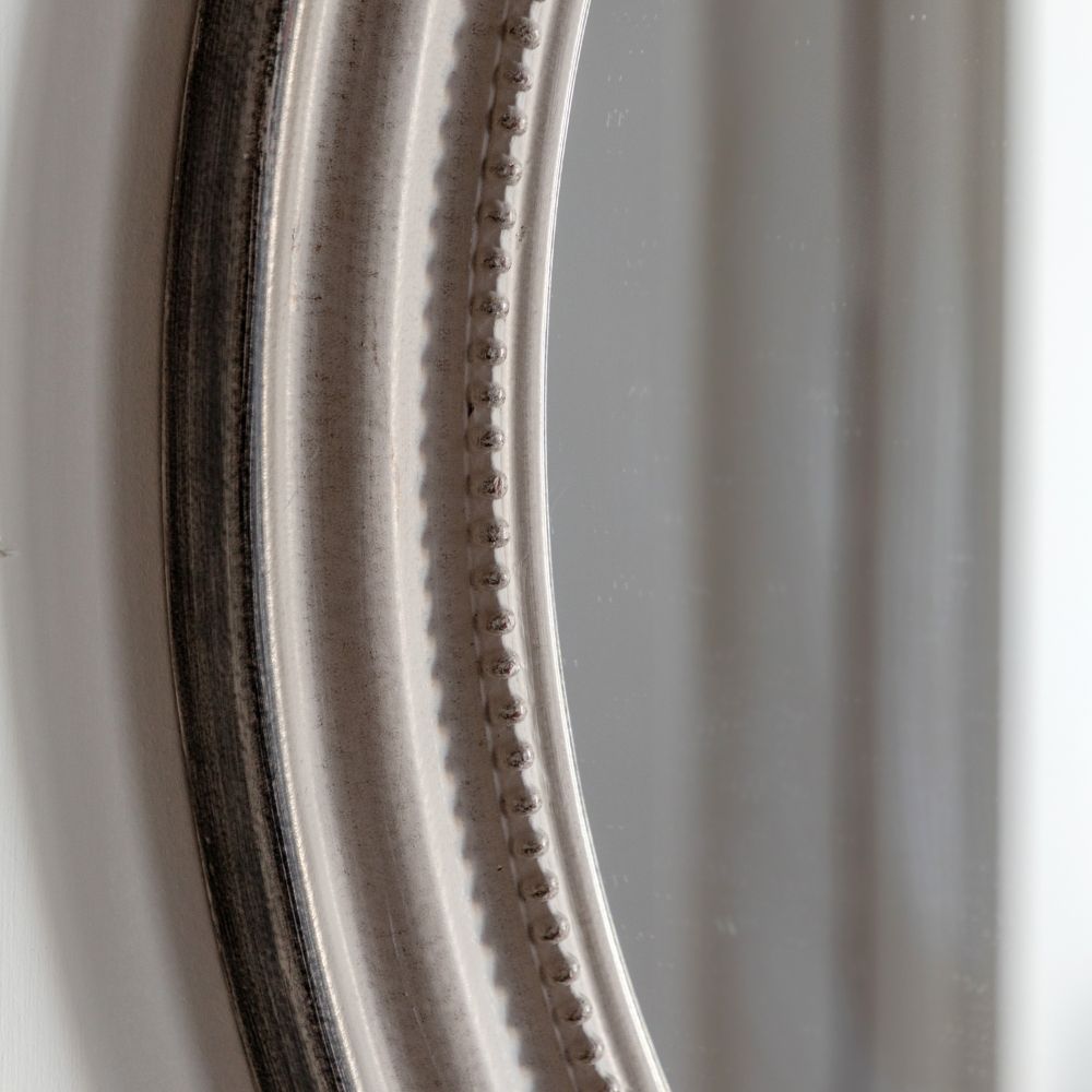 Close-up detail of a round distressed grey mirror frame featuring decorative beaded edging and antique style finish.