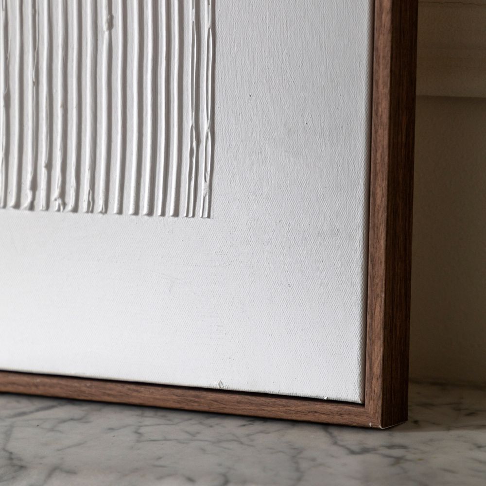 Close-up detail of textured white canvas artwork with raised linear design and slim dark wood frame.